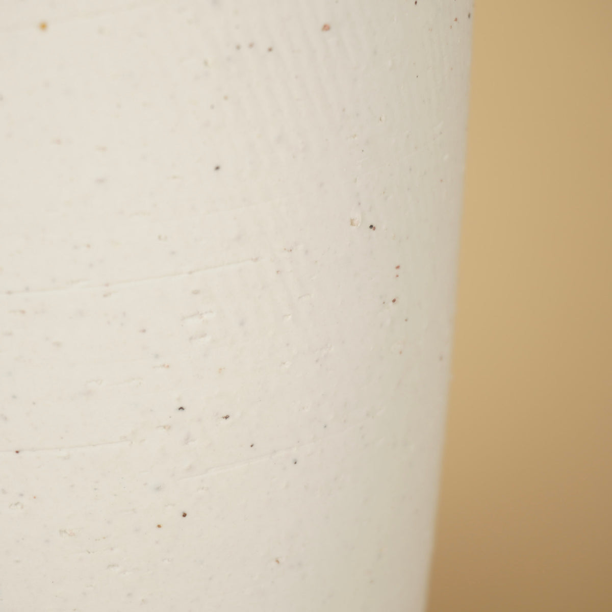 Detail van het matte, crèmekleurige oppervlak van de vaas met kleine donkere spikkels en fijne horizontale lijnen.