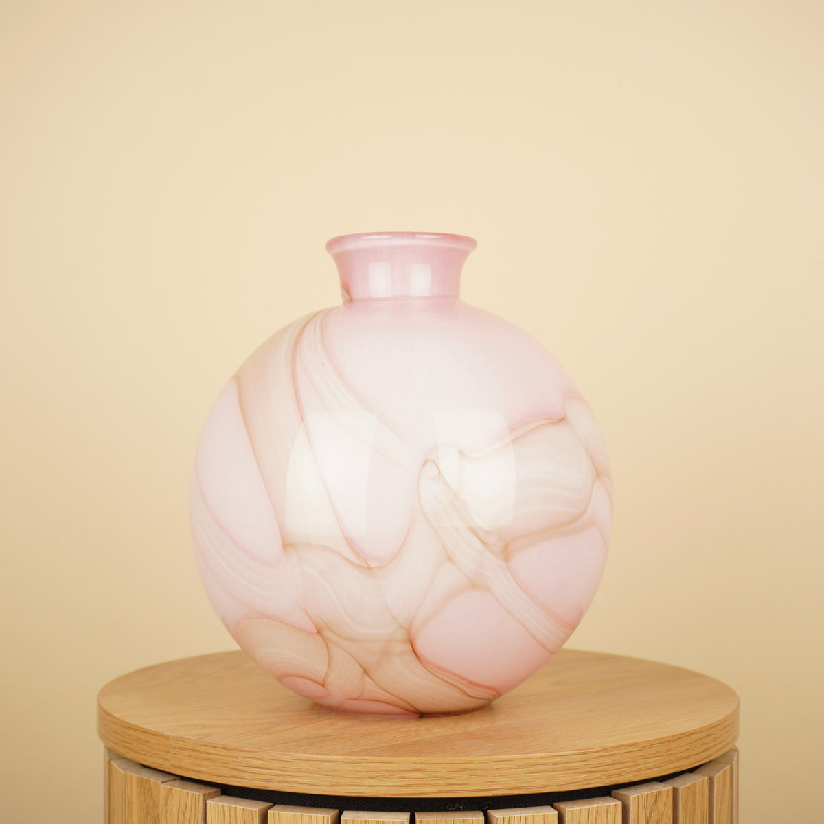 Ronde roze vaas met crème en beige marmerpatroon en korte hals op een houten tafel