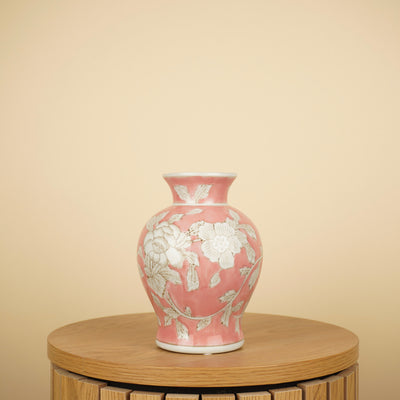 Roze vaas met witte bloemen en bladeren, een smalle hals en uitlopende rand op een ronde houten tafel.