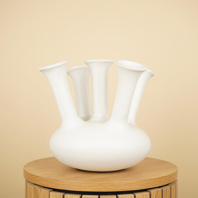 Witte tulpenvaas met ronde buik en vijf lange, uitlopende halzen op een ronde houten tafel.